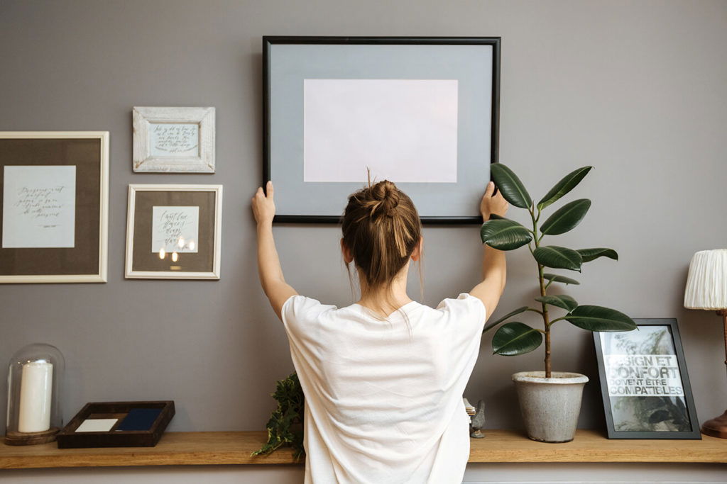 woman putting up picture frame to declutter her apartment